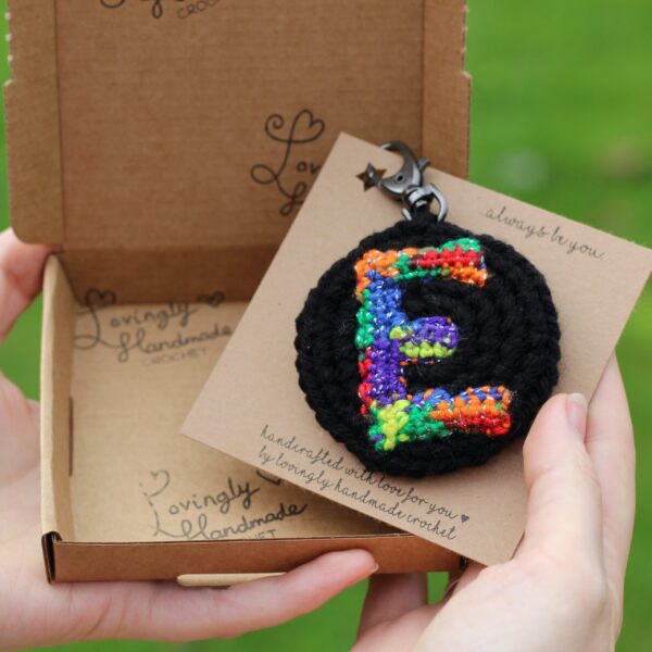 A personalised statement keyring featuring a rainbow letter of your choice set on a black background with a muted colour palette rainbow reverse.