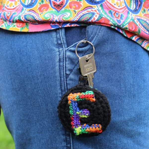 A personalised statement keyring featuring a rainbow letter of your choice set on a black background with a muted colour palette rainbow reverse.