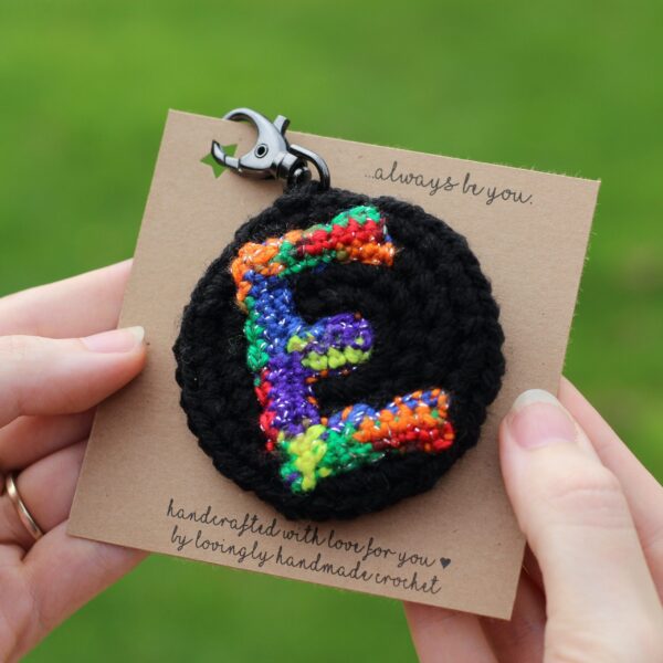 A personalised statement keyring featuring a rainbow letter of your choice set on a black background with a muted colour palette rainbow reverse.